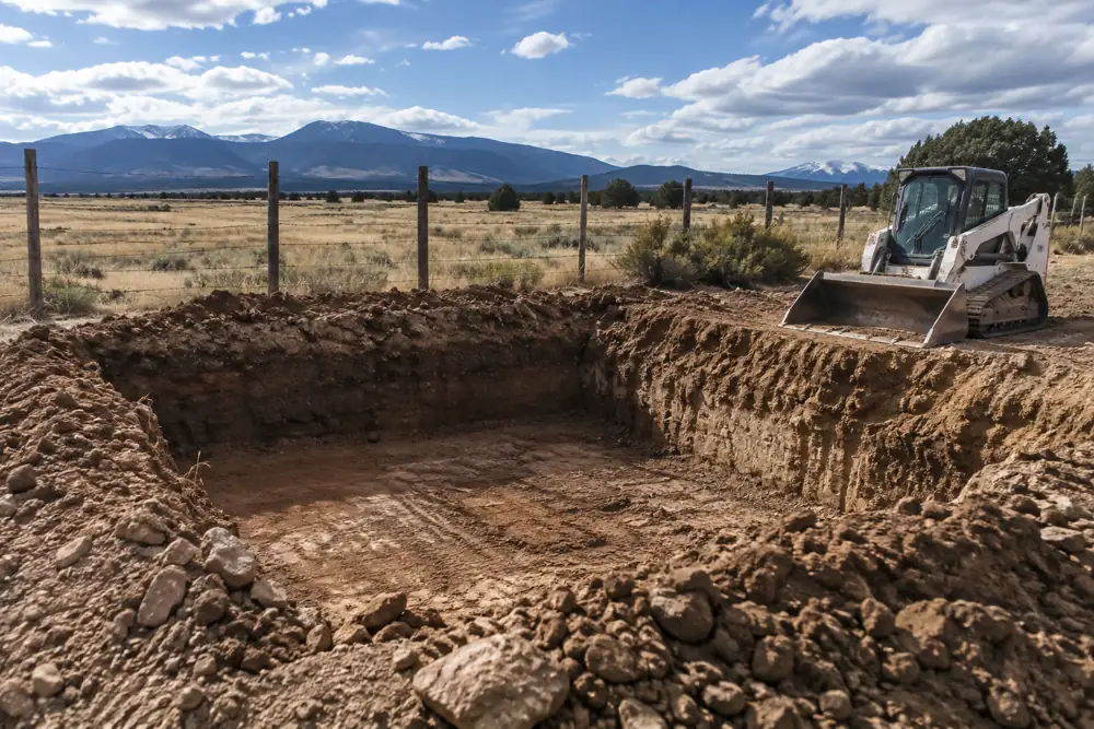 Freshly excavated pit and a skid steer on flat rural acreage